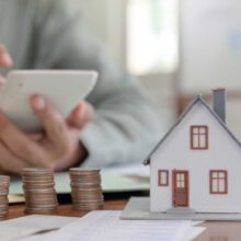 Estate Planning close up shot of houses models and coins with a mans hand on calculator