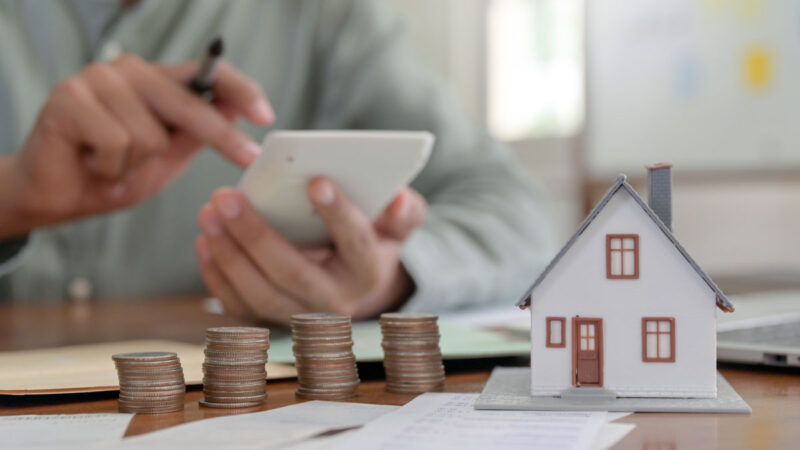 Man typing on calcalator at desk with money and a house statuette