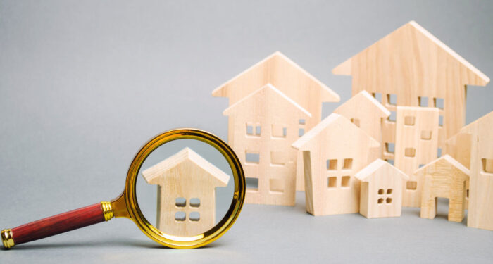 A magnifying glass over a little wooden house with other wooden houses in the background